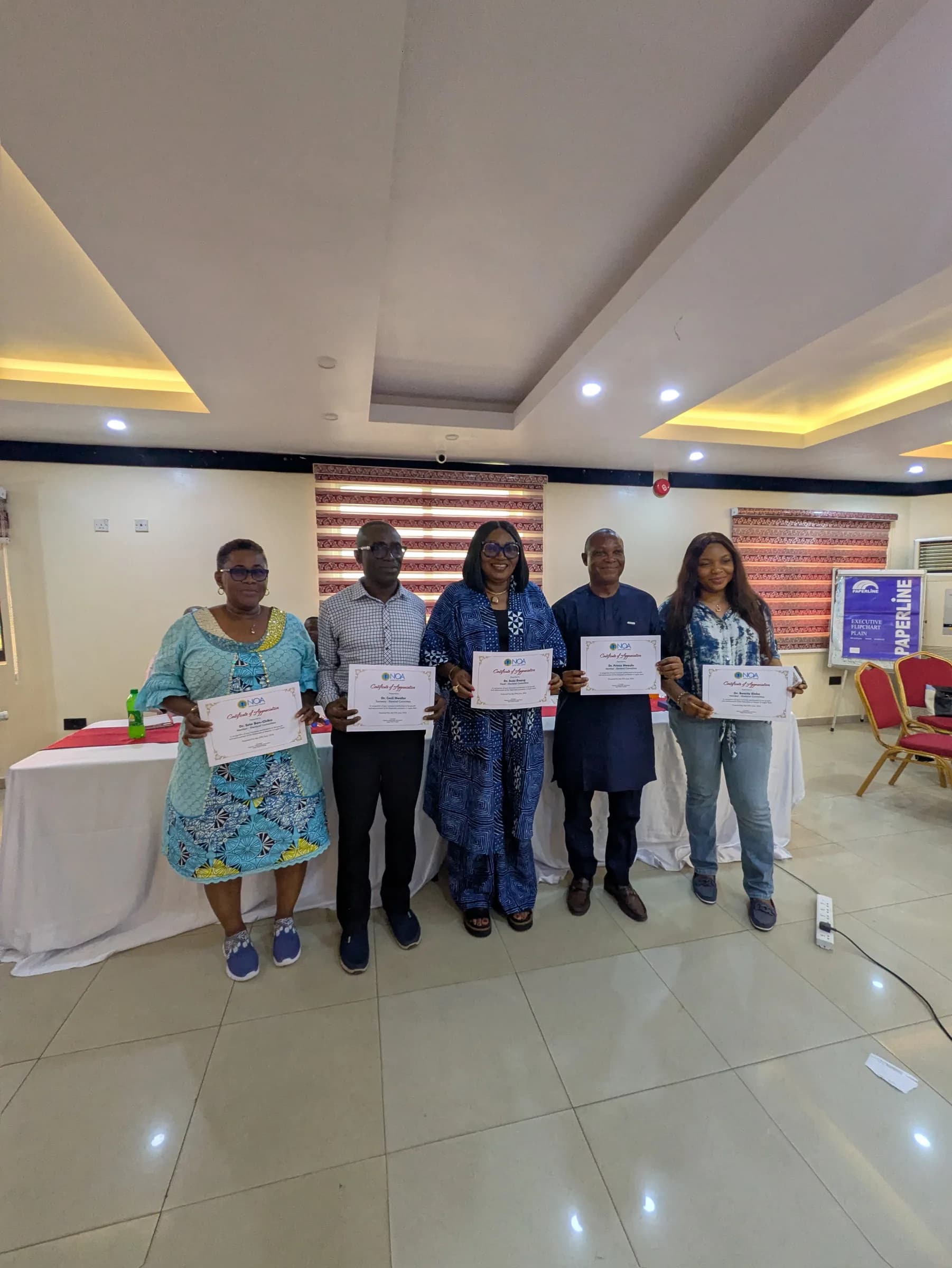 Five members standing in a hall, each holding a framed certificate.