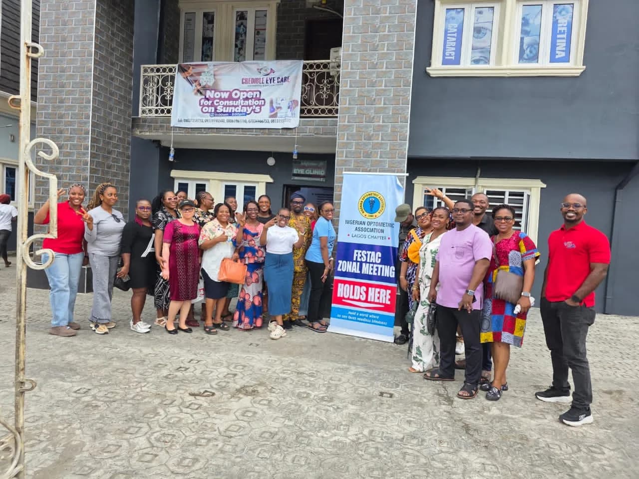 Members standing outside an eye clinic beneath a banner reading "Festac Zonal Meeting holds here".