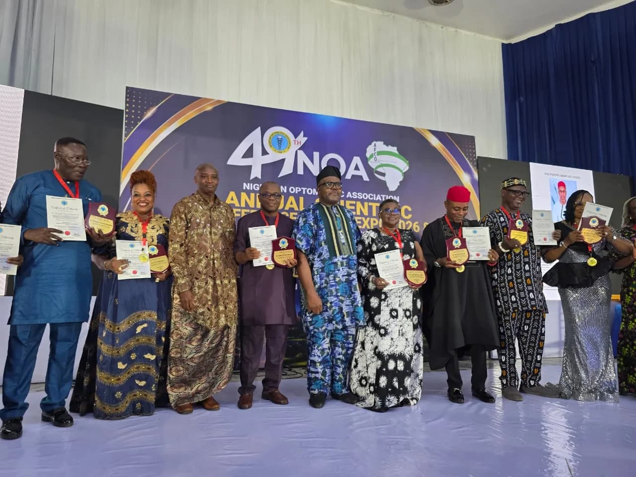 A line of recipients holding certificates and plaques in front of the conference backdrop.