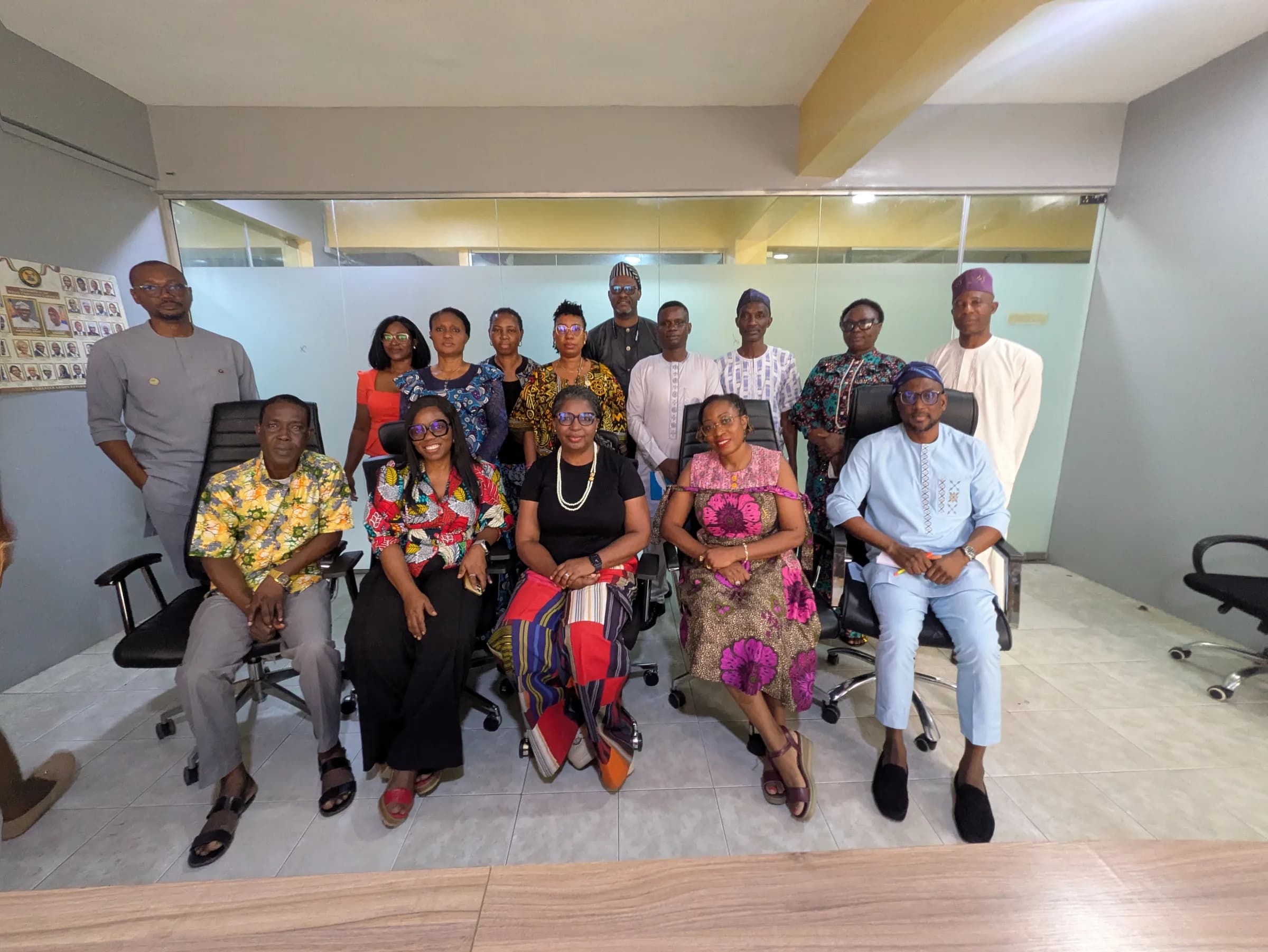 A seated group photograph of members in a meeting room, some standing behind.