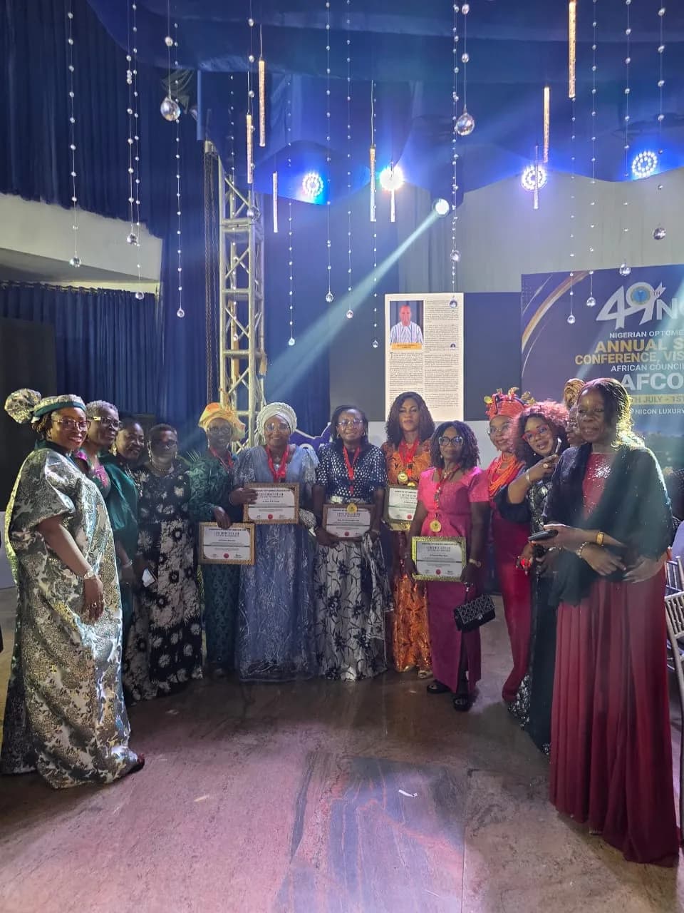Award recipients holding certificates on a stage under coloured lighting.