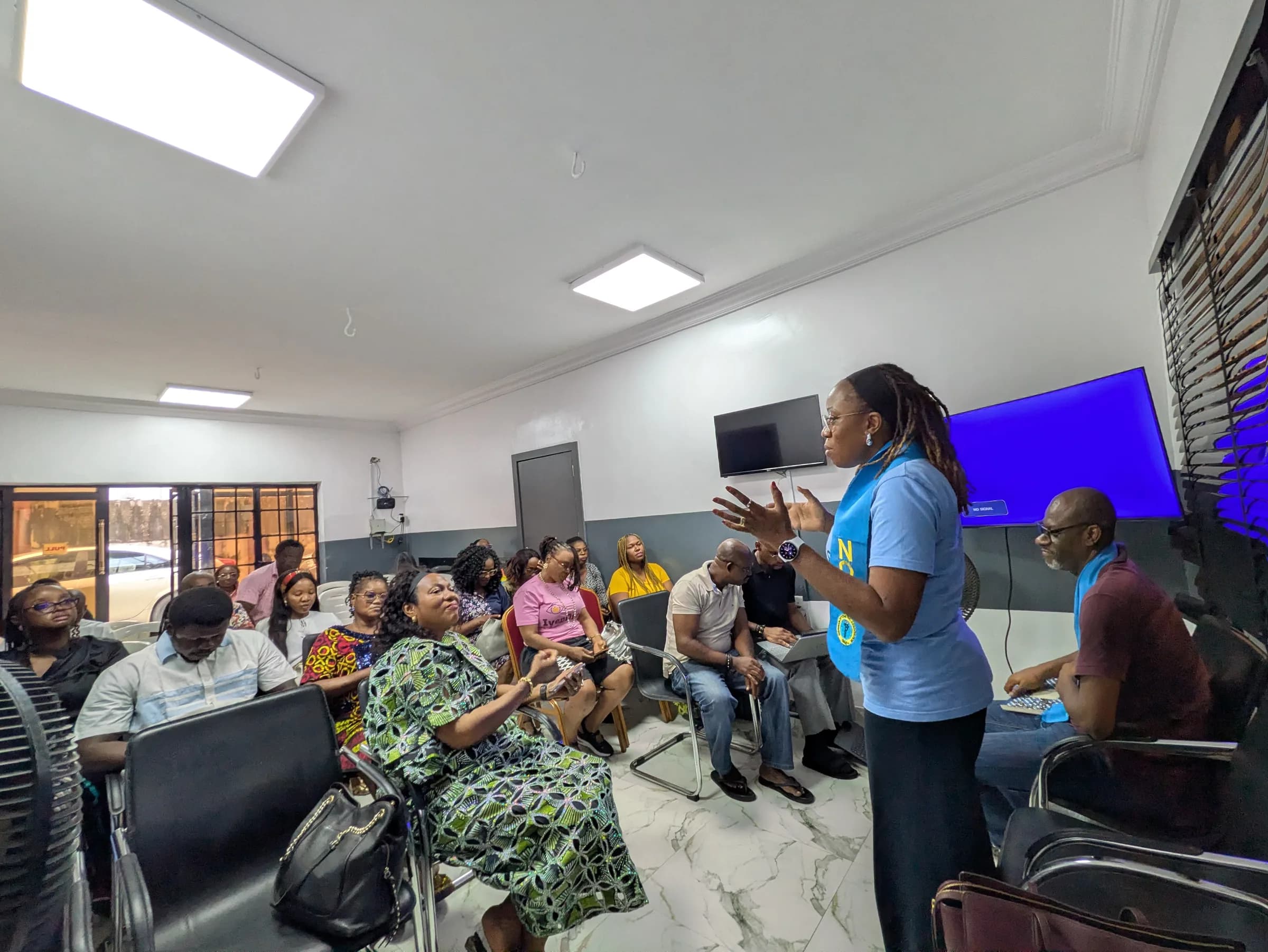 A member in a blue NOA shirt standing to give an eye-health talk to a seated audience.